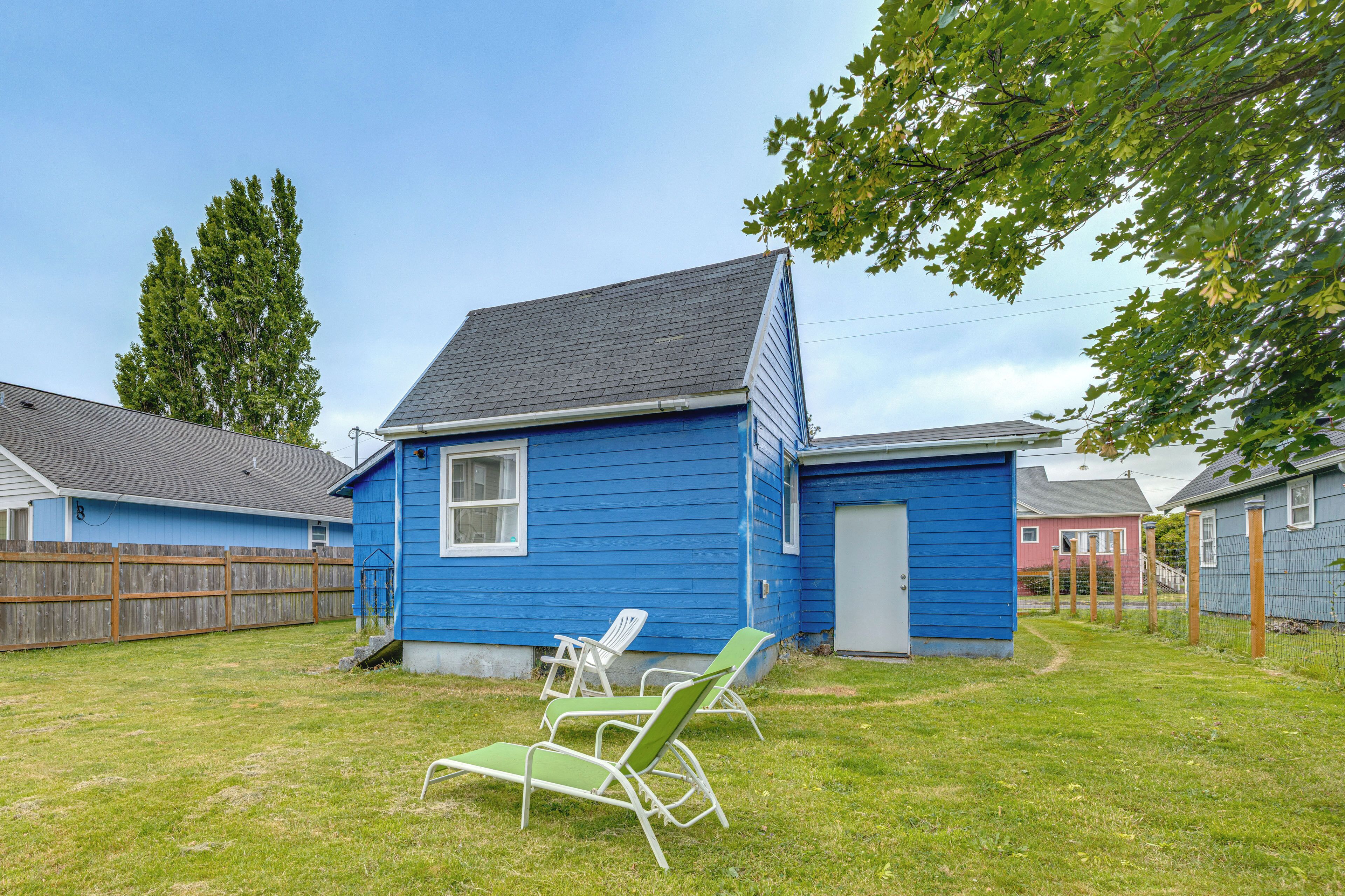 A blue house with a fenced yard, two lawn chairs, and a small shed.