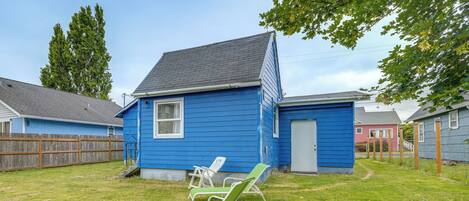 A blue house with a fenced yard, two lawn chairs, and a small shed.