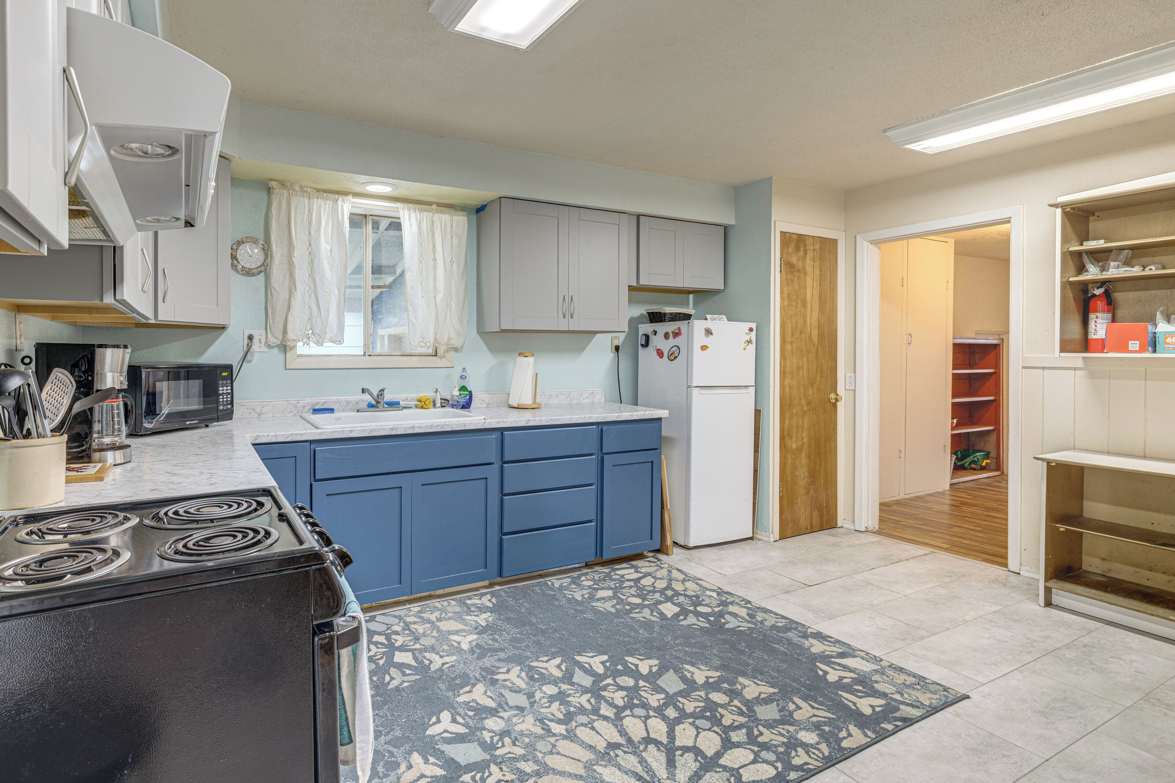 A kitchen with a stove, microwave, refrigerator, and blue cabinets.