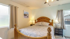 A bedroom with a wooden bed, a nightstand, a lamp, a window with curtains, and a painting on the wall. - Great for Families! Tillamook Getaway Near Beaches (Tillamook)