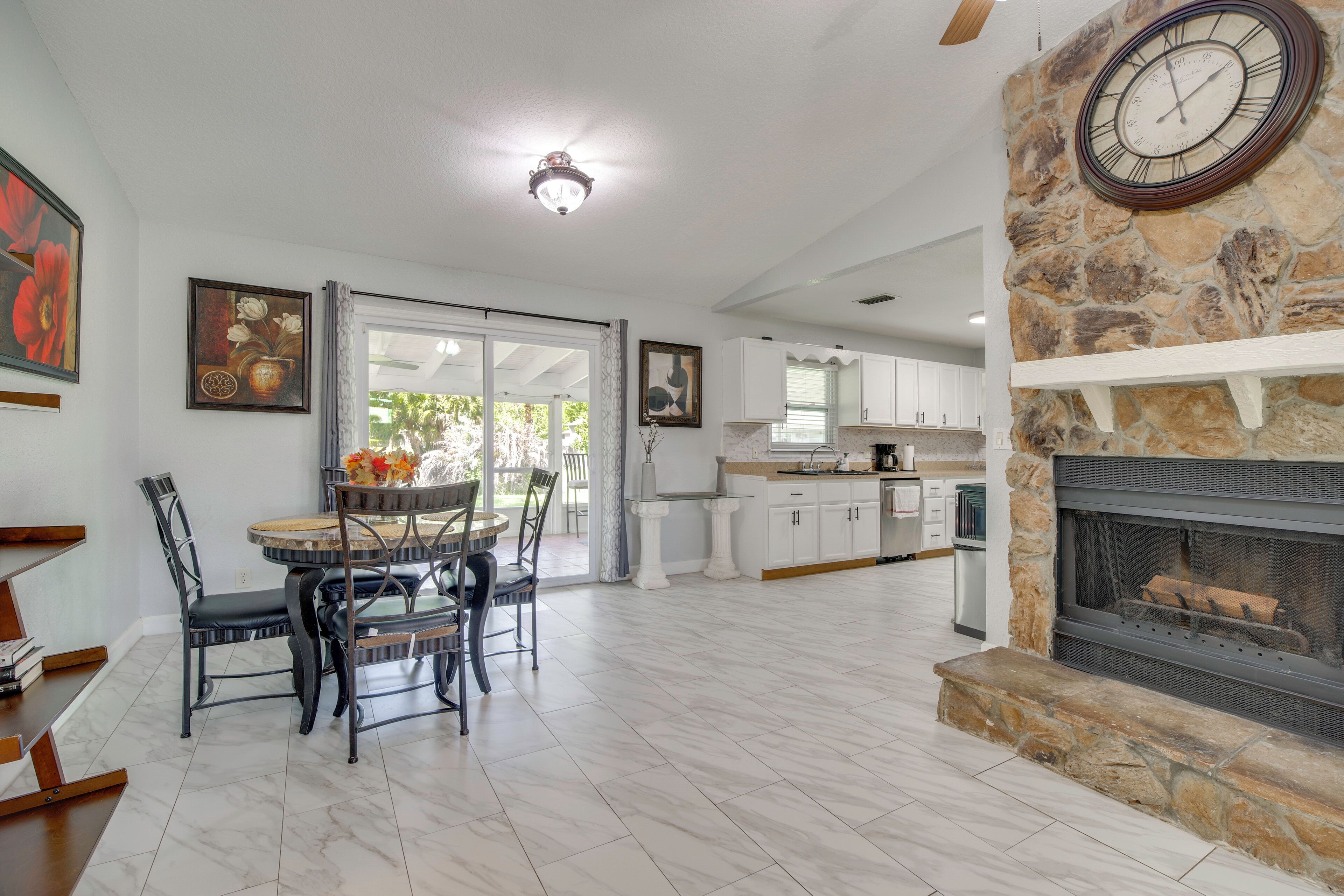 A spacious living area with a dining table, chairs, a stone fireplace, and a kitchen in the background.