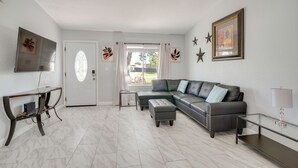Un salon comprenant un canapé d’angle, un téléviseur, une console et une porte avec une fenêtre.