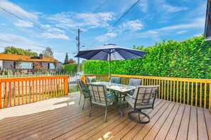 A wooden deck with a table and chairs, an umbrella, and a hedge in the background. - Work-friendly Seattle Retreat By Parks + Hospitals (Seattle)