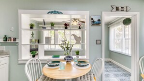 Un coin repas comprenant une table ronde en bois, des chaises blanches et une étagère blanche intégrée, agrémentée de divers objets décoratifs.