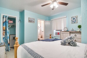 Une chambre à coucher avec un lit, une armoire, un ventilateur de plafond et une salle de bain visible à travers une porte ouverte.