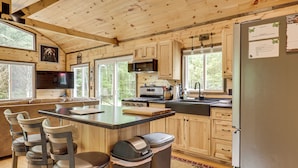 A wooden cabin kitchen with a large island, bar stools, a refrigerator, and a television. - Secluded Cabin w/ UTV Trail Access in Harshaw! (Harshaw)