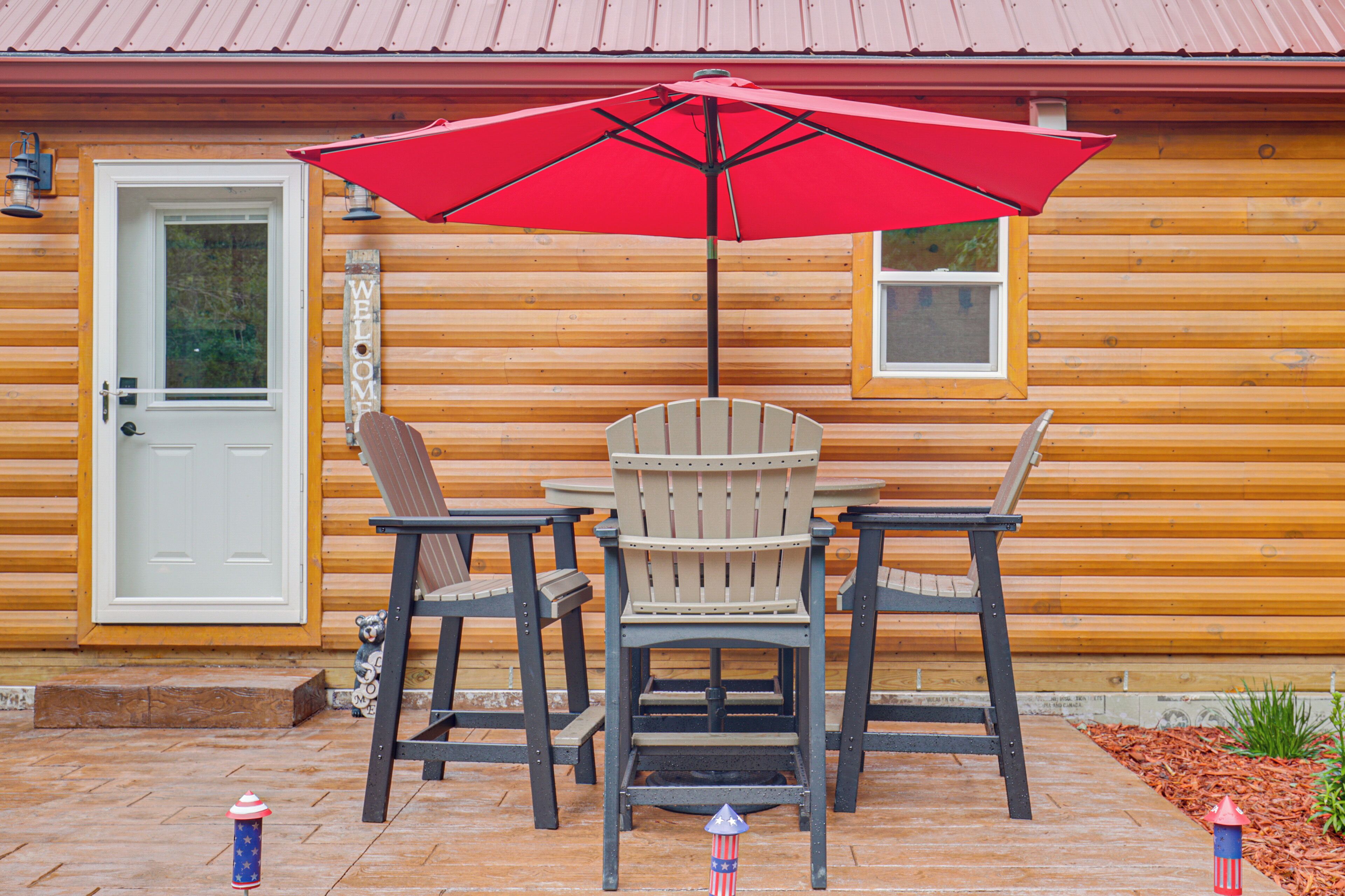 A wooden cabin with a red umbrella, a white door, and a welcome sign.