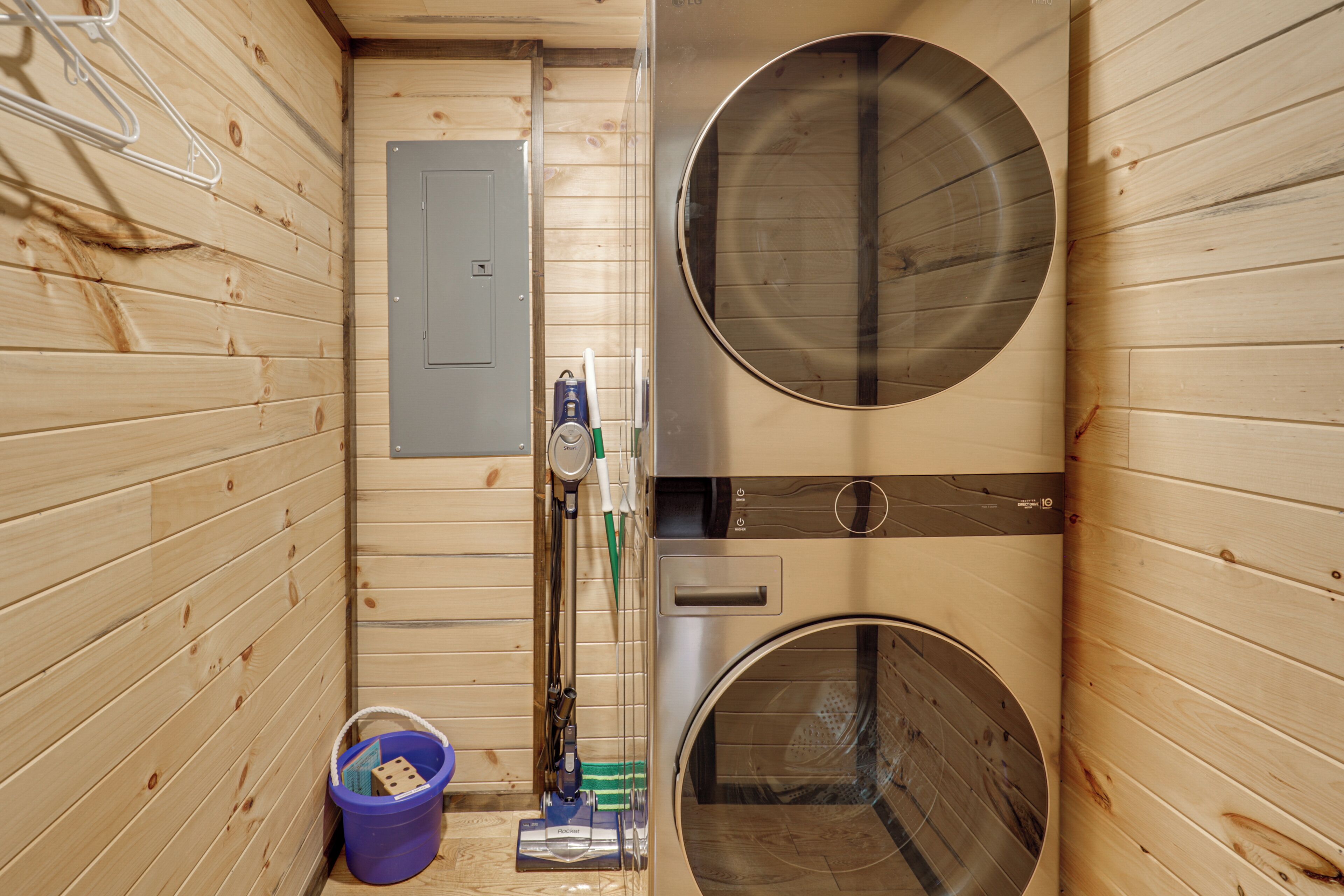 A sauna room with wooden walls, two large circular windows, a door, and a small bucket with items.