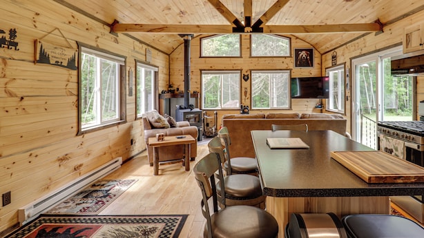 A cabin interior with a wooden interior, a sofa, a dining table, chairs, a kitchen area, and large windows. - Secluded Cabin w/ UTV Trail Access in Harshaw! (Harshaw)