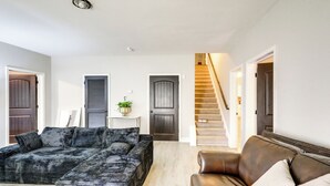 Een woonkamer met een donkere gestreepte bank, een bruine leren bank, en een trap die naar een hoger niveau leidt.