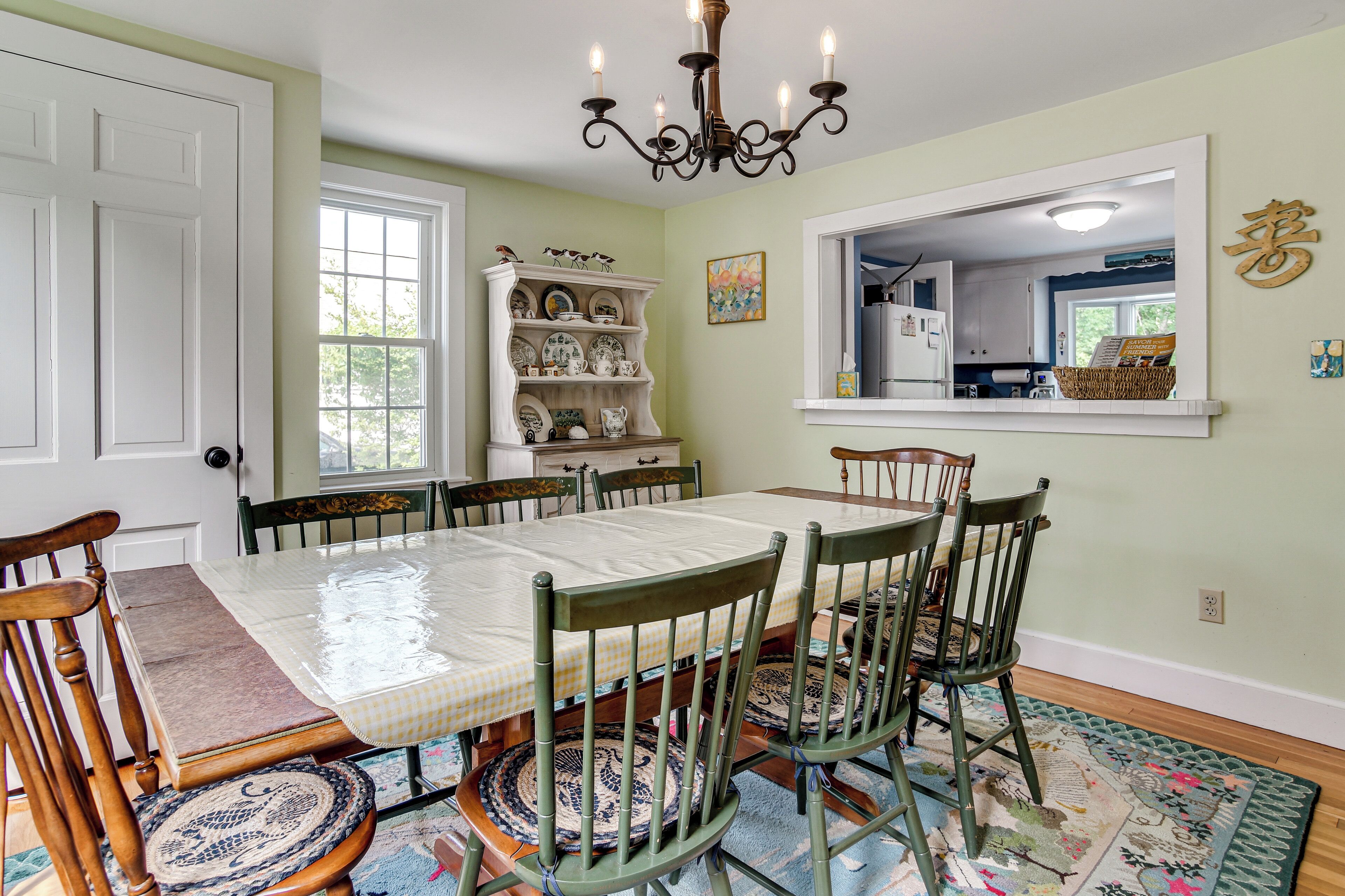 A dining room with a table set for six, surrounded by chairs, a chandelier, a window, and a built-in shelf with dishes.