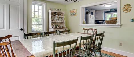 A dining room with a table set for six, surrounded by chairs, a chandelier, a window, and a built-in shelf with dishes.