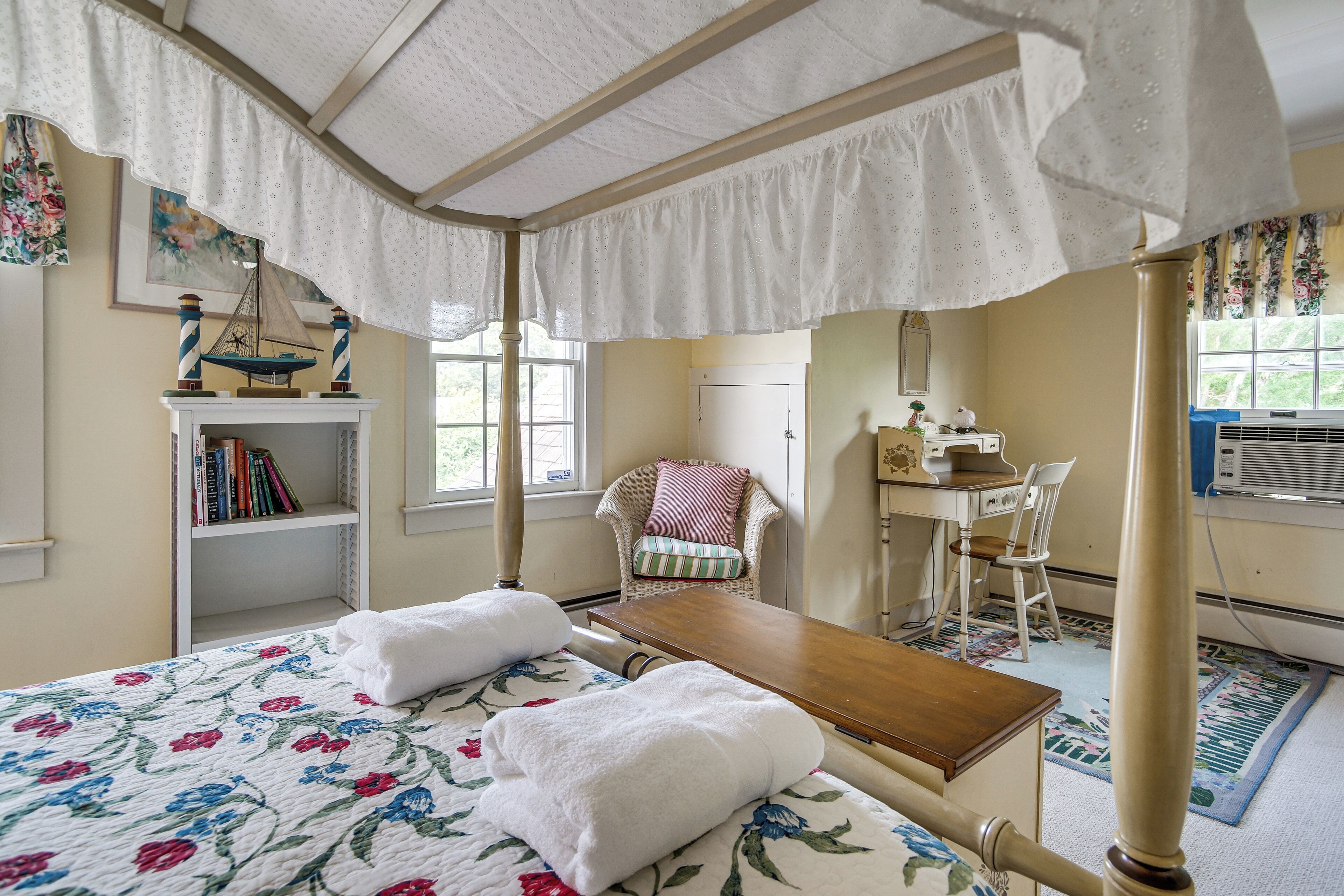 A room with a bed, a wooden table, a chair, a bookshelf, and a window.