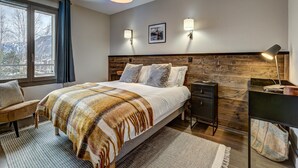 Ein modernes Schlafzimmer mit einem großen Bett, Nachttischlampen, einem hölzernen Kopfteil und Blick ins Freie durch das Fenster.