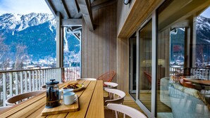 Eine Holzterrasse mit Tisch und Stühlen mit Blick auf eine verschneite Berglandschaft.