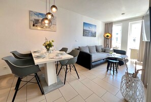 A modern living room with a dining area, grey sofas, a coffee table, and a lamp. - Ostseeurlaub mit Stil - Moderne Ferienwohnung in Sellin (Sellin)