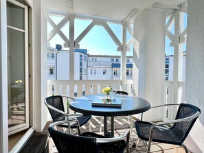 Un balcon avec une table ronde et quatre chaises, une porte vitrée et une vue sur les immebles.