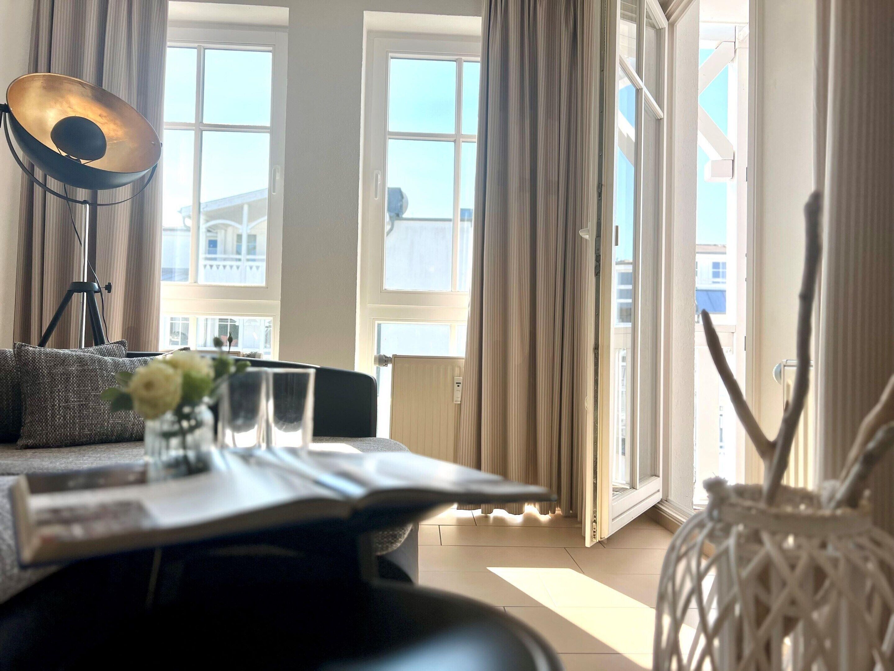 A room with a dining table, chairs, a lamp, and a view of buildings through large windows.