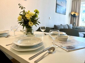 Ein Esstisch gedeckt mit Tellern, Gläsern und Besteck, eine Vase mit Blumen und einer Zeitschrift.