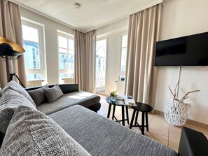 A modern living room with a sofa, a coffee table, and a TV mounted on the wall. - Ostseeurlaub mit Stil - Moderne Ferienwohnung in Sellin (Sellin)