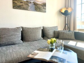 Ein modernes Wohnzimmer mit einem grauen Sofa, einer Stehlampe und einer Zeitschrift auf dem Couchtisch.