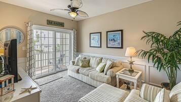A living room with a striped sofa, a television, a ceiling fan, and a large window with a view of the outside.