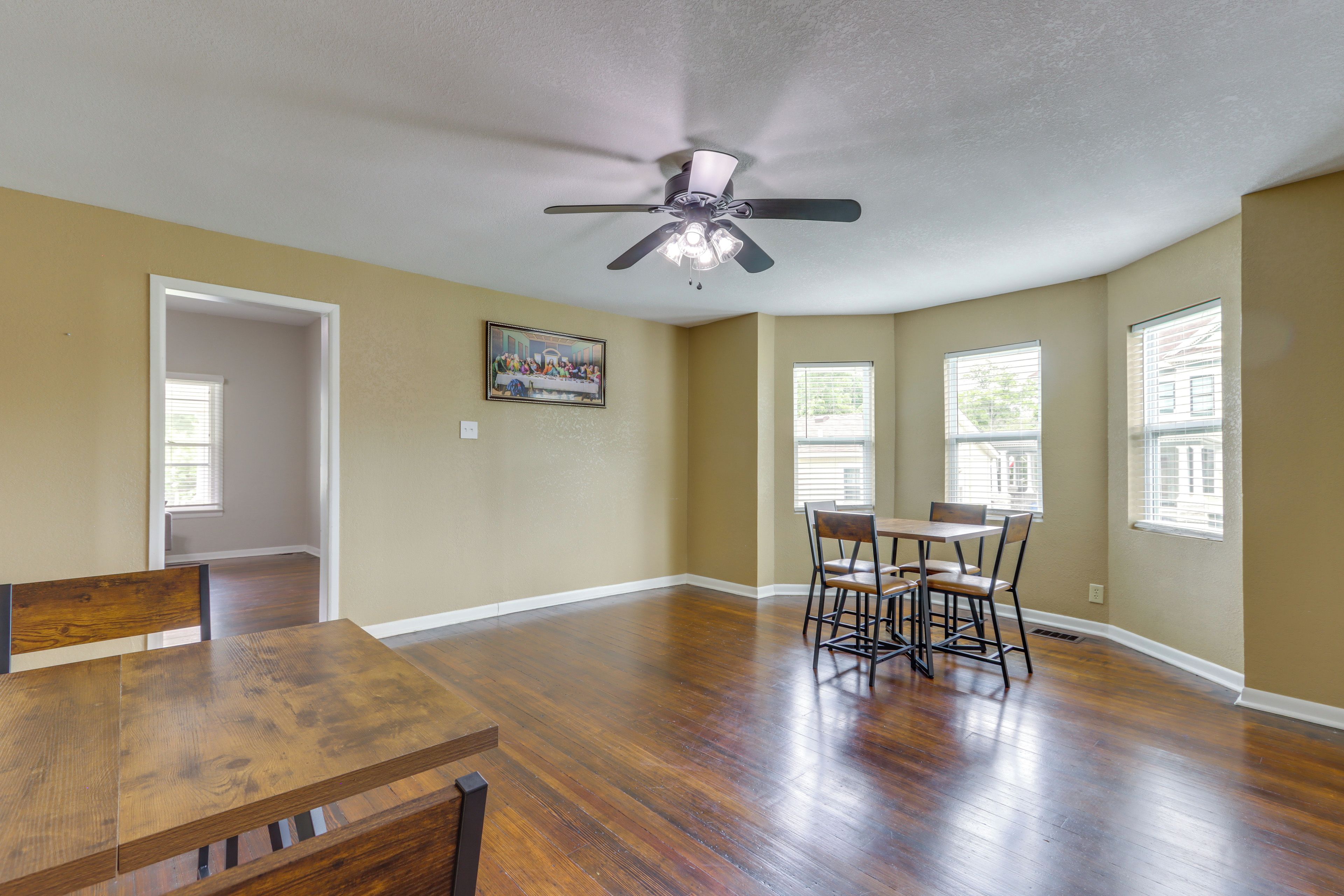 A spacious room with hardwood floors, a ceiling fan, and a dining table with chairs.