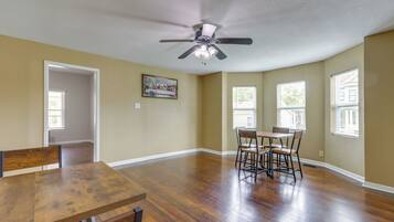 A spacious room with hardwood floors, a ceiling fan, and a dining table with chairs.