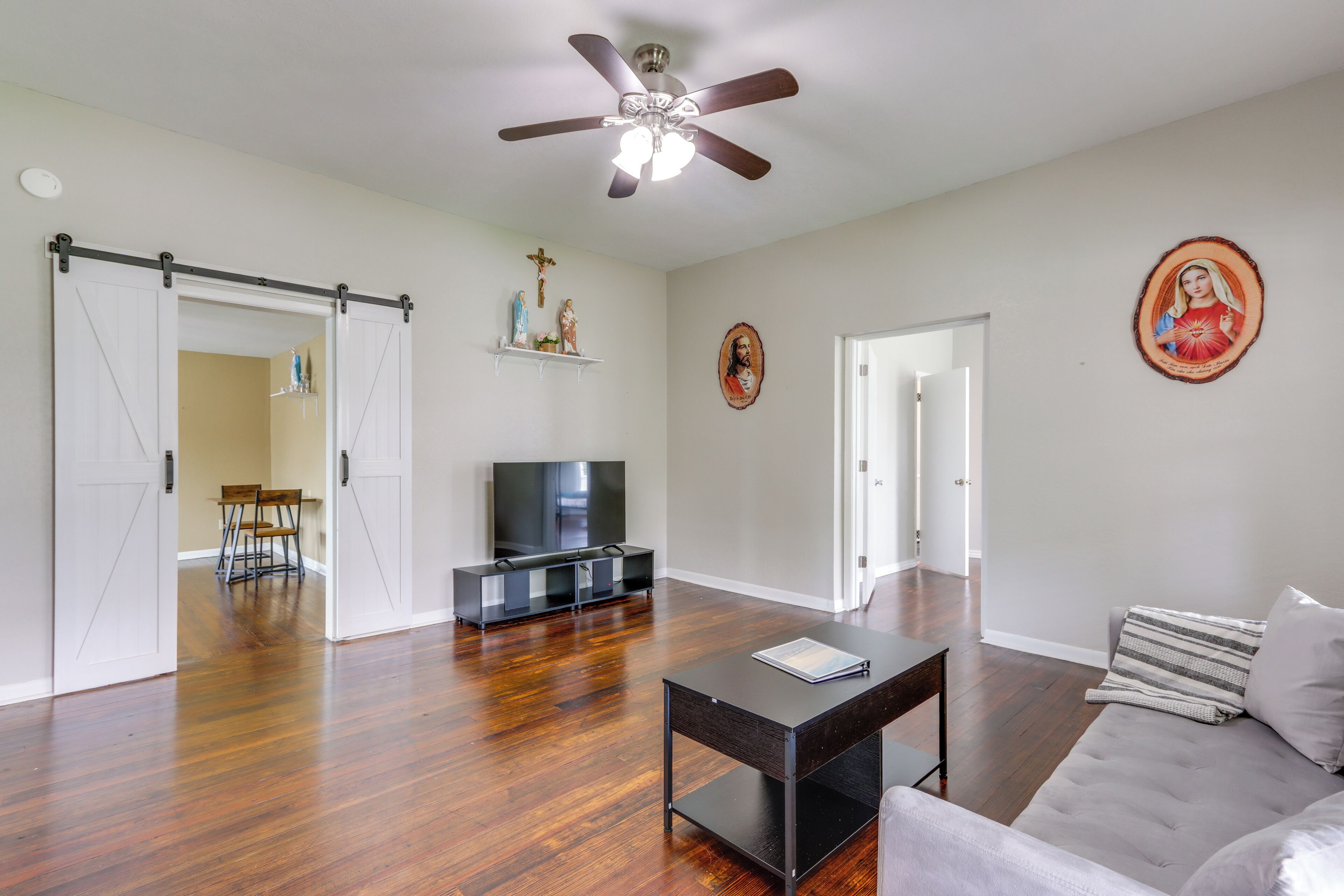 A spacious living room with hardwood flooring, a ceiling fan, a flat-screen TV, a sofa, and a coffee table.