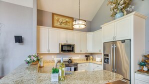 A kitchen with white cabinets, a granite countertop, stainless steel appliances, and a hanging light fixture.