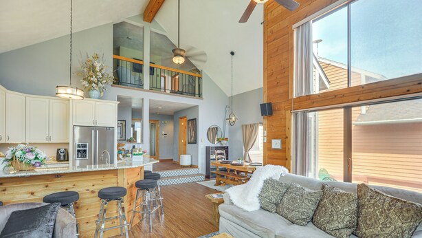 A spacious living area with a high ceiling, a kitchen with a central island, and a cozy seating area with a sofa and bar stools.
