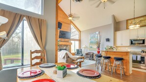 A dining area with a wooden table set for four, a kitchen with modern appliances, and a large window with curtains.