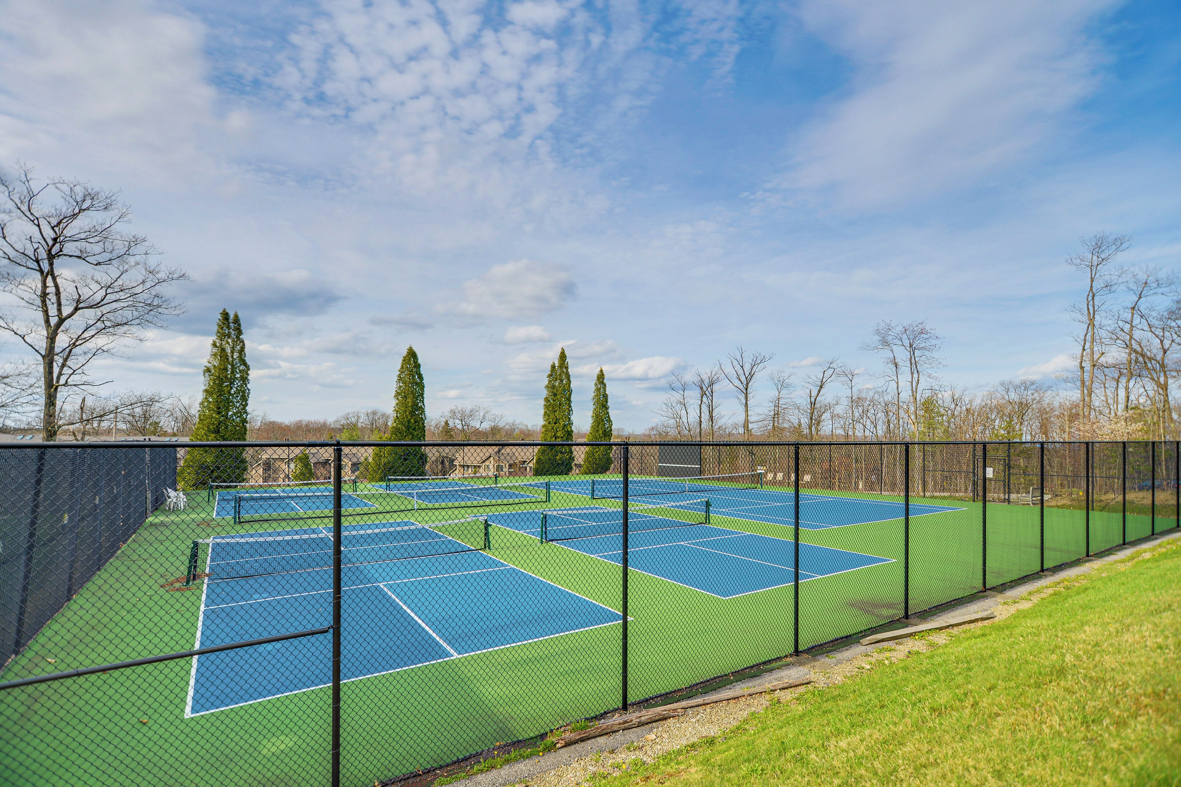 Ein Tennisplatzkomplex mit mehreren Plätzen, umzäunt und mit Bäumen im Hintergrund.