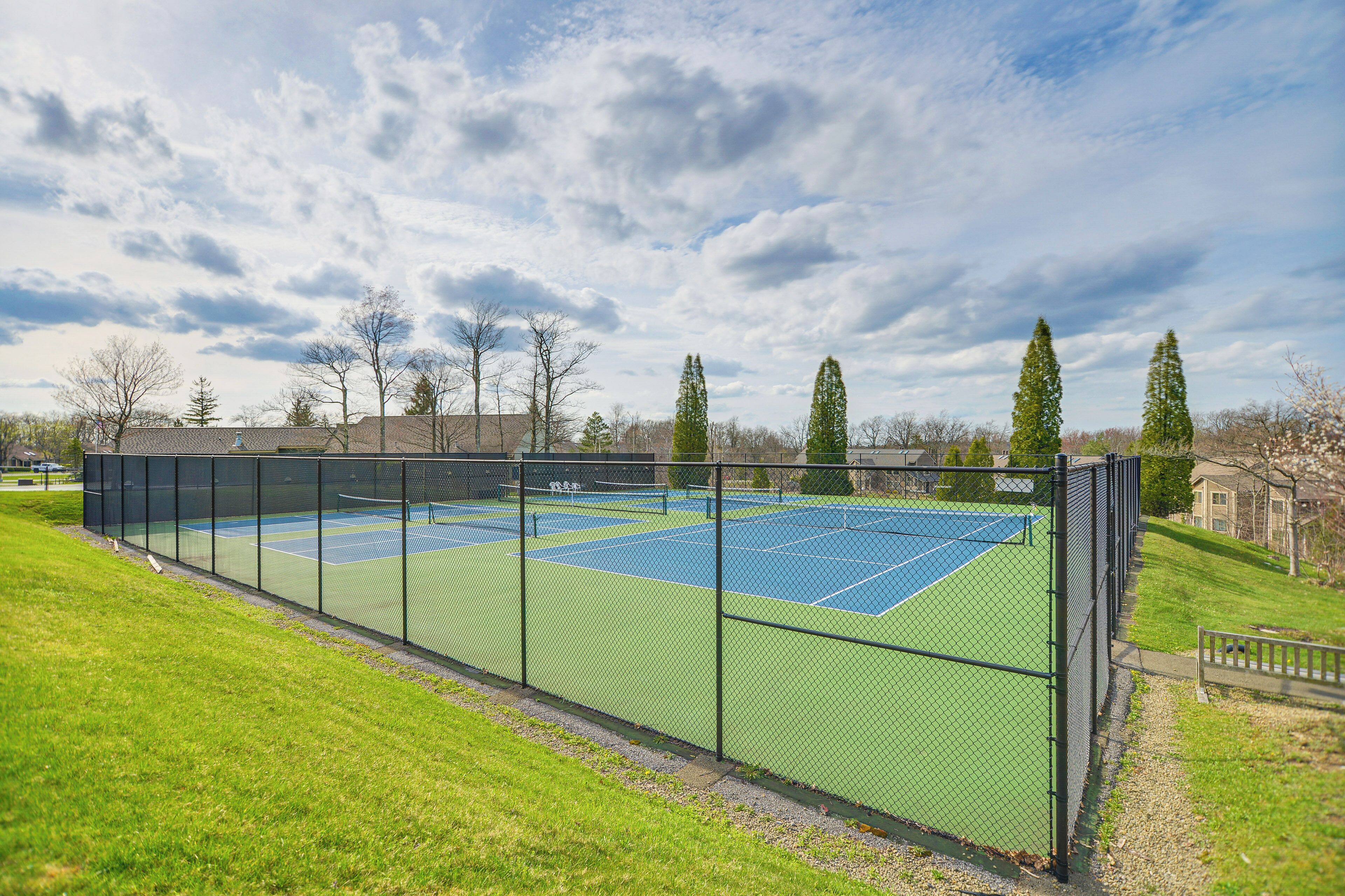 Ein Tennisplatz mit Netz, umgeben von einem Zaun und Bäumen im Hintergrund.