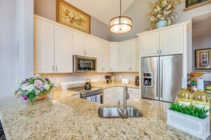 A kitchen with white cabinets, stainless steel appliances, granite countertops, and a hanging light fixture.