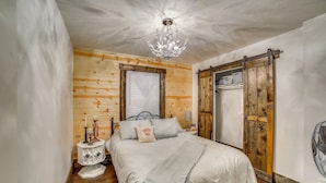 Een slaapkamer met een bed, een kroonluchter, houten wanden, een schuifdeur en een ventilator.
