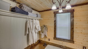 Een kamer met houten lambrisering, een wit schap waarop handdoeken liggen en een kledingrek met witte badjassen.