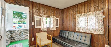 Une pièce avec des murs en bois, un mur en pierre, un canapé, un fauteuil et une fenêtre avec des rideaux.