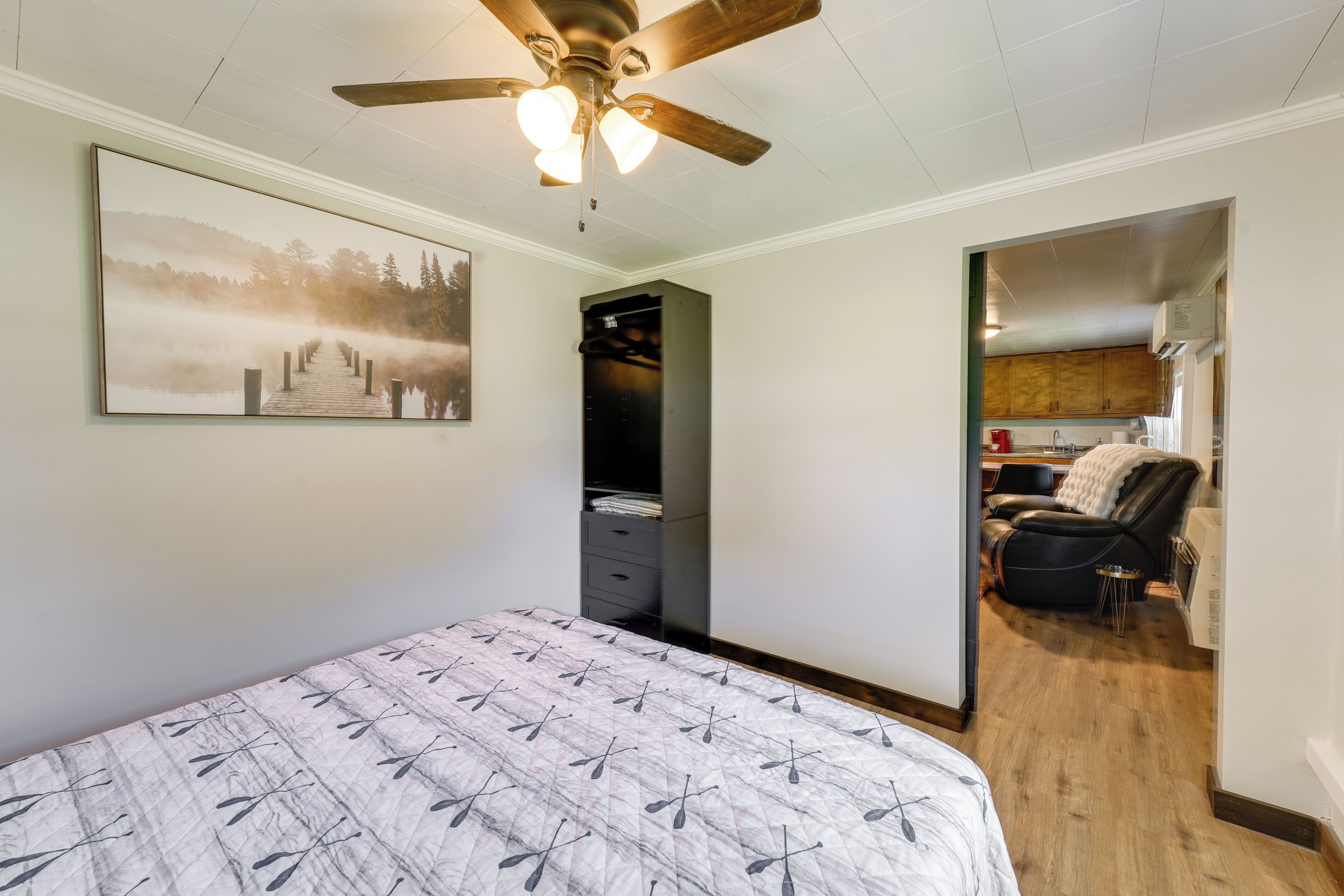 A bedroom with a bed, a ceiling fan, a wardrobe, and a view into the kitchen area.