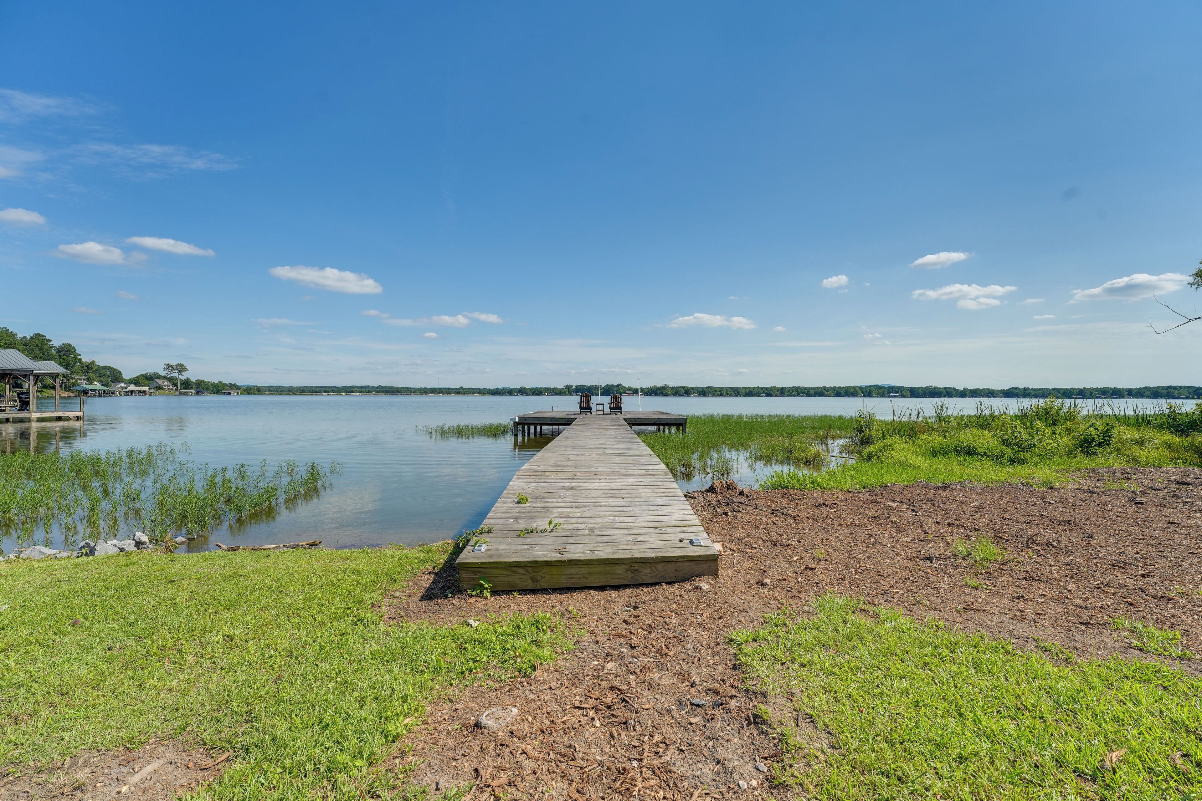 A wooden dock extending into a calm lake, surrounded by grassy areas and a clear sky.