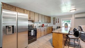 A kitchen with stainless steel appliances, wooden cabinets, a bar area with stools, and a window providing natural light. - 'cast a Line Cabin' w/ Dock on Weiss Lake (Centre)