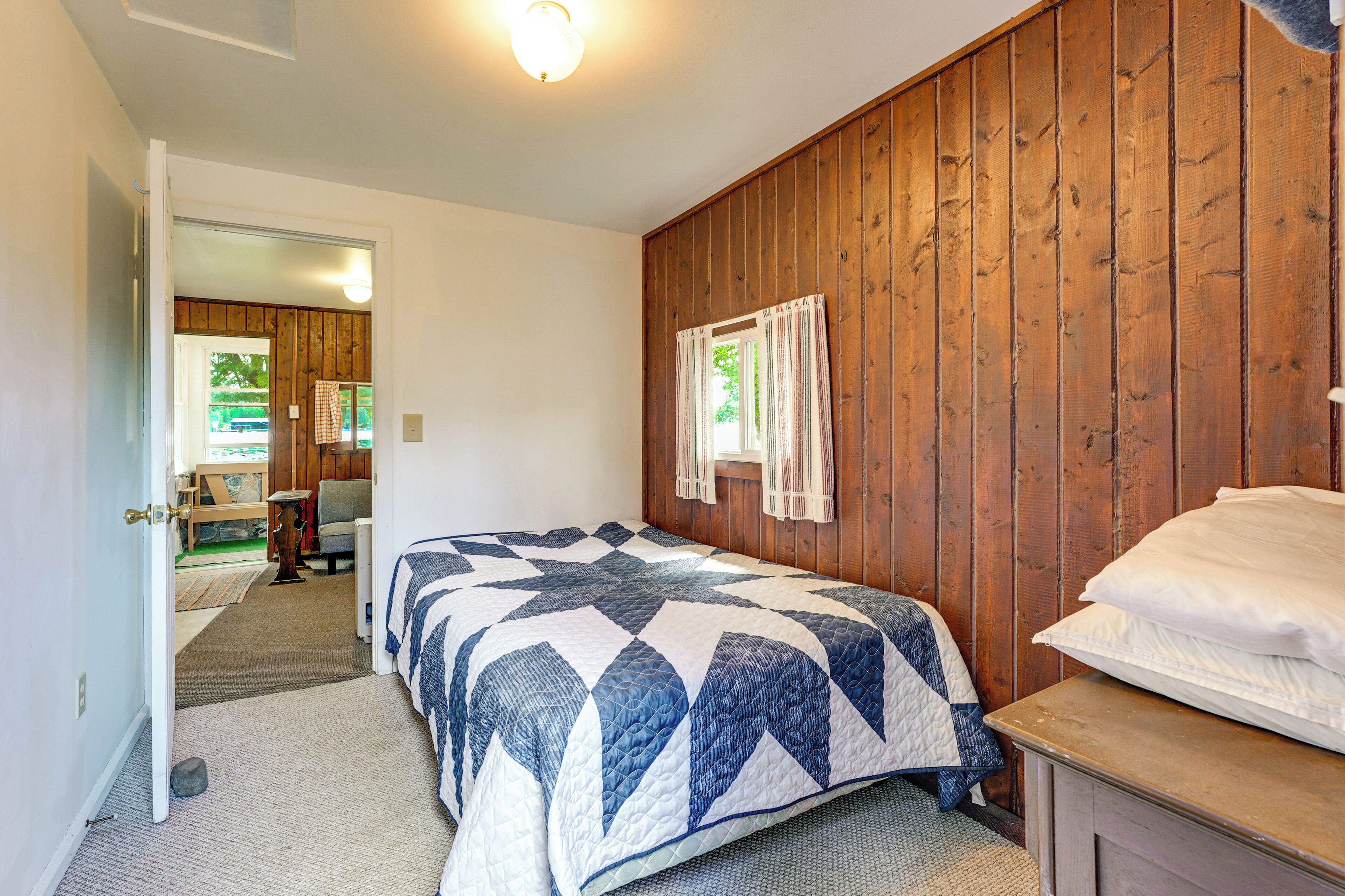 Ein Schlafzimmer mit Holzwand, einem Bett mit Patchworkdecke, einem Nachttisch und einer Tür zu einem anderen Raum.