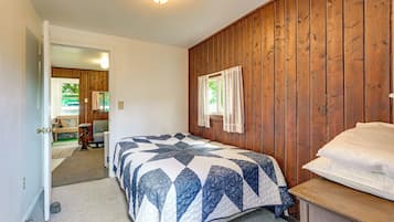 Ein Schlafzimmer mit Holzwand, einem Bett mit Patchworkdecke, einem Nachttisch und einer Tür zu einem anderen Raum.