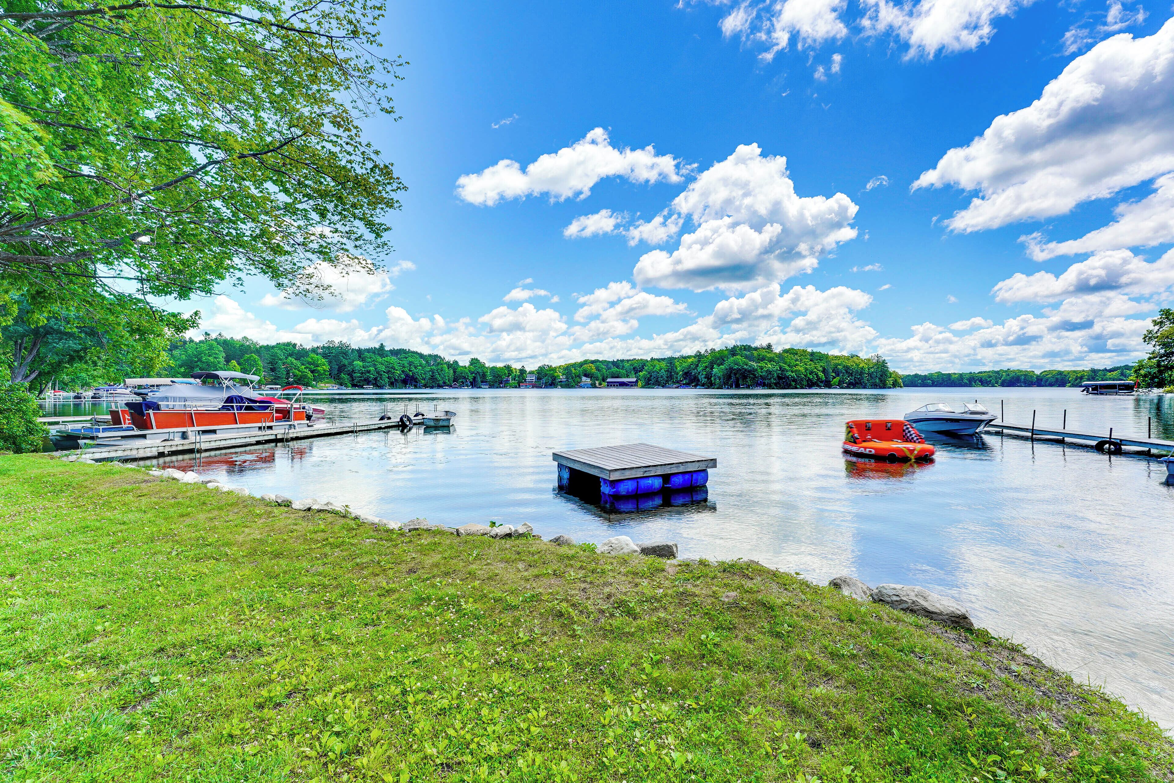 A calm lake with boats docked, a grassy shore, and a clear sky.