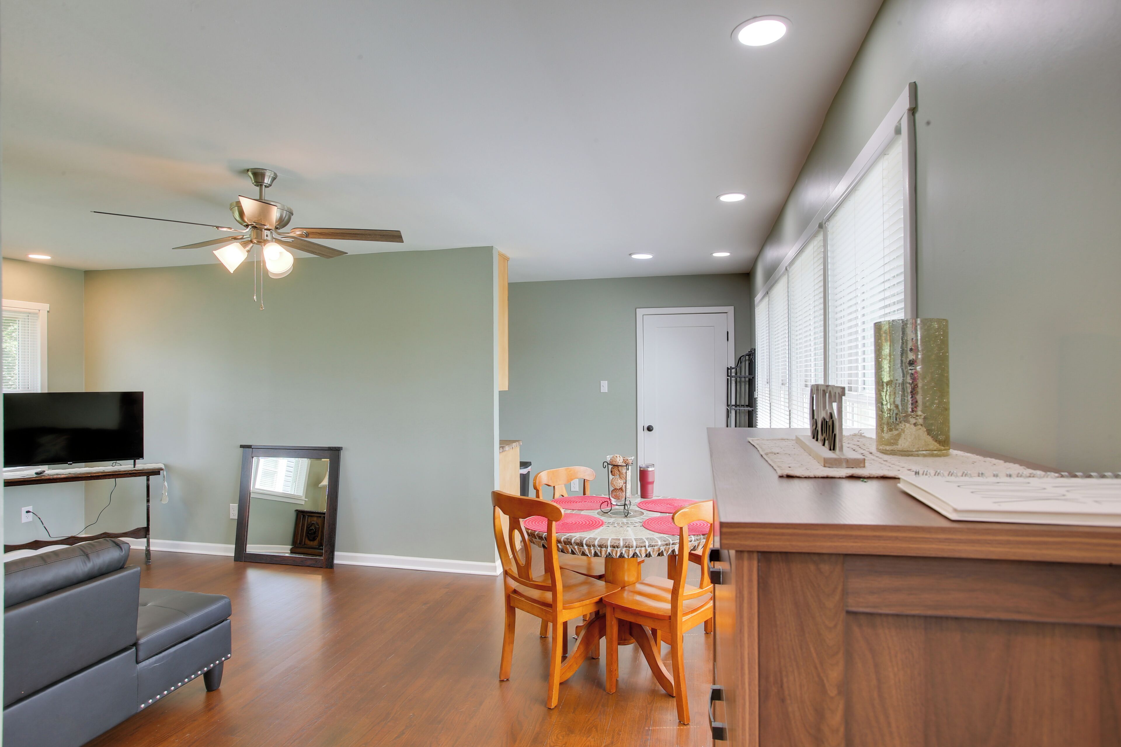 A living room with a sofa, a dining table with chairs, a ceiling fan, and a television.