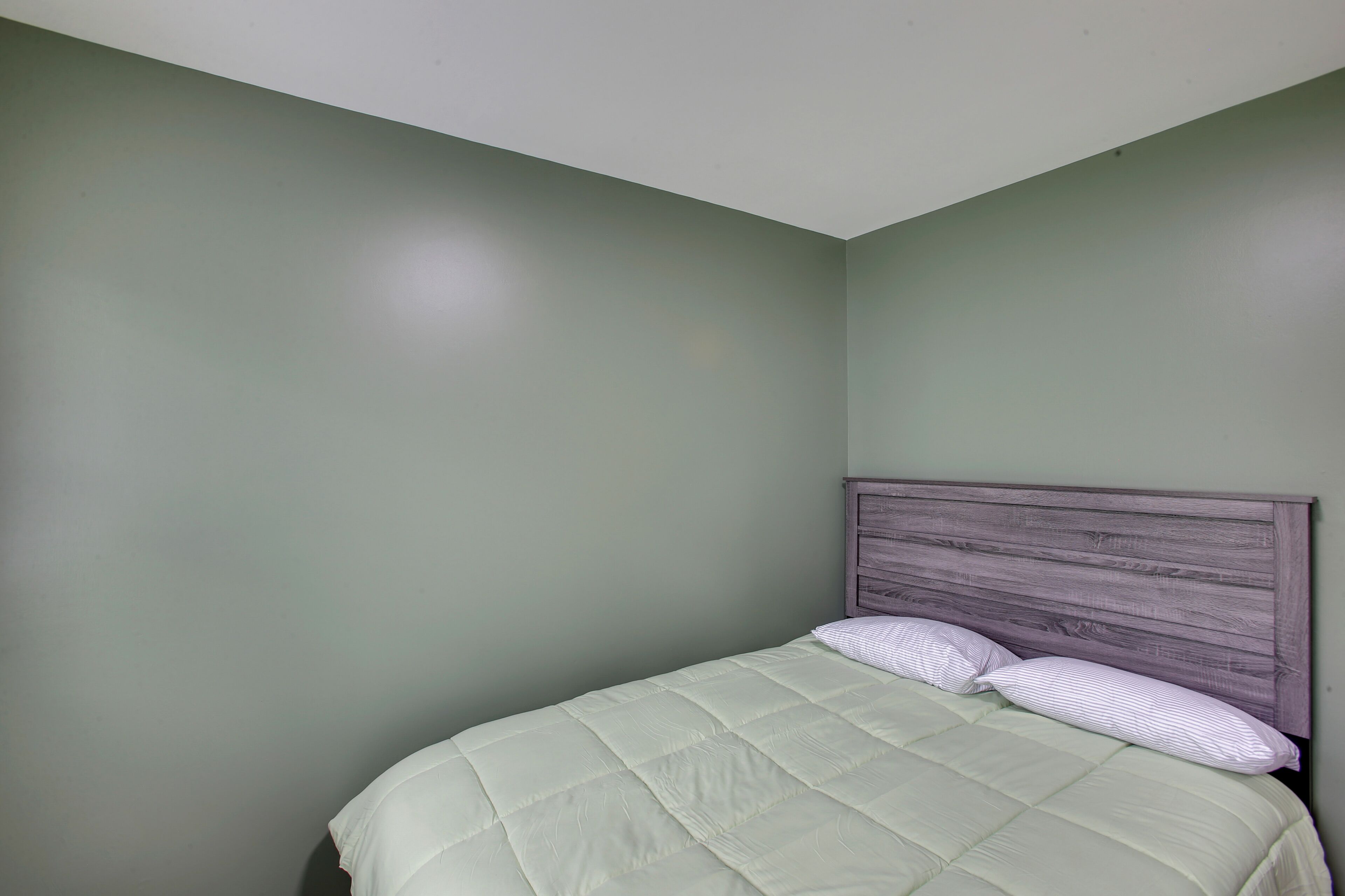 A single bed with a wooden headboard, a green wall, and a white ceiling.