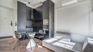 A modern kitchen with dark cabinetry, a glass dining table, and a grey sofa. - New! Luxury Old town apartment (Vilnius)