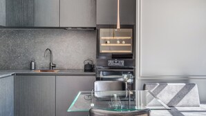 A modern kitchen with a glass-top table, stainless steel appliances, and a built-in oven. - New! Luxury Old town apartment (Vilnius)