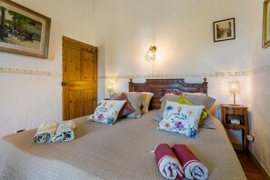 Une chambre avec une porte en bois, deux tables de chevet avec des lampes, un lit avec des coussins à motifs floraux et un tableau au mur.