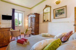Ein Hotelzimmer mit Bett, Sessel, Schrank, Fernseher und einem Gemälde an der Wand.